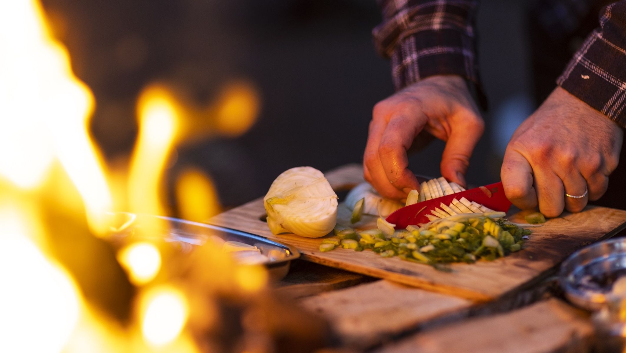 En man skär i tunnbrödmackor i ljuset av elden på Björnö. Foto: Henrik Trygg