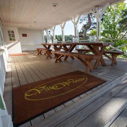 A mat reading 'Villa Wolax' lies on the floor of a terrace, which also features a long wooden table and a sea view.