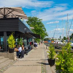 Boats line the riverbank at the Turku Guest Harbour, while diners enjoy a meal at NOOA.