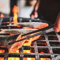 A person grills three fillets of fish over an open flame at Kakolanruusu.