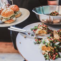 A waiter carries three different plates at Roster Turku, featuring burgers and salads.